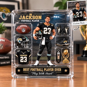 Könnte beinhalten: Eine durchsichtige Vitrine mit einer Footballspieler-Figur im schwarzen Trikot mit der Nummer 23, umgeben von Miniaturzubehör wie Football, Helm, Handschuhen, Stollen, Pfeife und Trophäe. Text: JACKSON FOOTBALL PLAYER und BEST FOOTBALL PLAYER EVER Play With Heart.