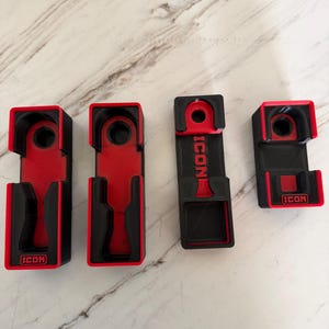May include: Four black and red plastic tool organizers with a rectangular shape and cutouts. Each piece features the word ICON embossed in red lettering. The organizers have a hollow interior design with a circular hole at the top end.