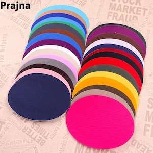 May include: A collection of circular fabric patches arranged in two overlapping stacks. The patches feature a wide variety of solid colours including bright pink, yellow, red, navy blue, white, purple, and various shades of grey, brown, and green.