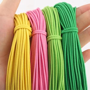 May include: Four bundles of elastic cord in bright yellow, pink, light green, and dark green. Each bundle is neatly tied with a matching piece of cord, showcasing a smooth, rounded texture and consistent thickness across all four vibrant colors.