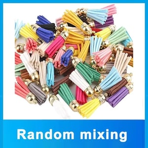 May include: A large collection of small, multi-coloured faux suede tassels, each featuring a shiny gold-toned metal cap with a small loop at the top. The tassels are presented in a variety of vibrant colours including yellow, blue, pink, green, white, and brown.
