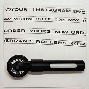 Op de afbeelding: Een zwart handmatig rolgereedschap met een cirkelvormig wiel met de tekst BRAND ROLLERS. Het gereedschap is geplaatst op een witte kaart bedrukt met de tekst @YOUR INSTAGRAM, WWW.YOURWEBSITE.COM, ORDER YOURS NOW en @BRAND ROLLERS.