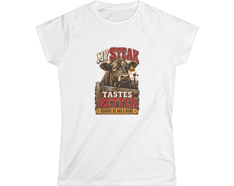 May include: A white short-sleeved t-shirt featuring a graphic of a brown cow behind a wooden fence. The text reads MY STEAK TASTES BETTER BECAUSE HE HAD A NAME, with the name EARL on an ear tag. The design uses red, brown, and yellow colors.