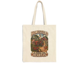 May include: A beige canvas tote bag featuring a colorful graphic of a farm scene with a red tractor, a goat, a chicken, and a house. The text reads HOMESTEAD IS WHERE THE HEART IS, with small red hearts flanking the bottom line of the printed design.