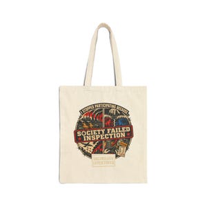 May include: A beige canvas tote bag featuring a circular graphic design with the text "I STOPPED PARTICIPATING BECAUSE..." and "SOCIETY FAILED INSPECTION" in the center. The illustration depicts industrial pollution, a puppet master, and financial documents.