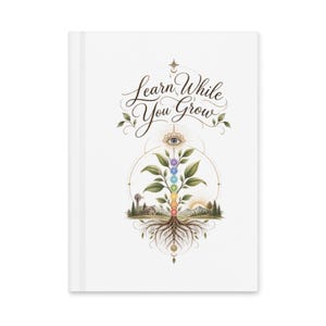 May include: A white hardcover journal featuring the text Learn While You Grow in elegant script. The design includes a central plant with seven colored chakra circles on its stem, roots extending downward, and a landscape with a house and sun.