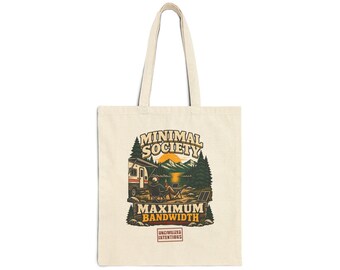May include: A cream-colored canvas tote bag featuring a graphic illustration of a person sitting in a chair by a camper near a lake and mountains. The text reads MINIMAL SOCIETY MAXIMUM BANDWIDTH and UNCIVILIZED INTENTIONS in a rectangular box.