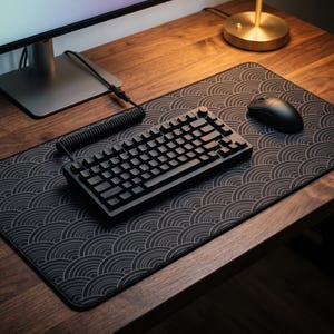 May include: A black mechanical keyboard with a coiled cable and a black computer mouse resting on a large rectangular desk mat featuring a repeating gray circular wave pattern. The keyboard has a knob on the top right corner and black keycaps.