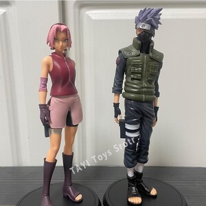 May include: Two anime character figures standing on circular black bases. The left figure has short pink hair, a maroon sleeveless top, and a light pink skirt. The right figure has spiky purple hair, a black face mask, and a green tactical vest.