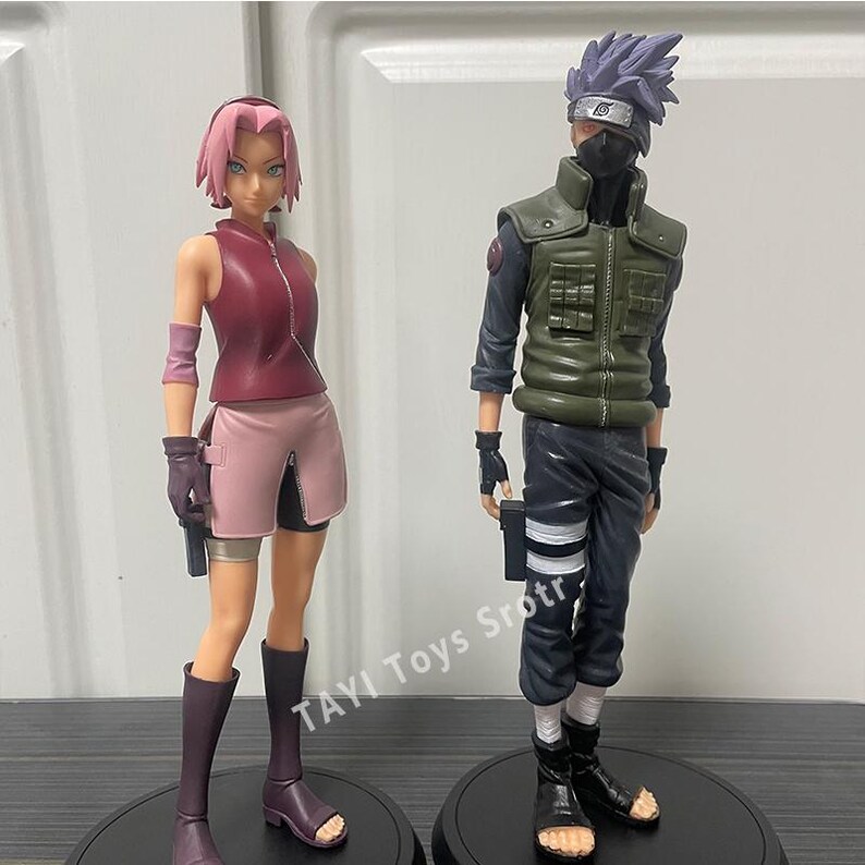 May include: Two anime character figures standing on circular black bases. The left figure has short pink hair, a maroon sleeveless top, and a light pink skirt. The right figure has spiky purple hair, a black face mask, and a green tactical vest.