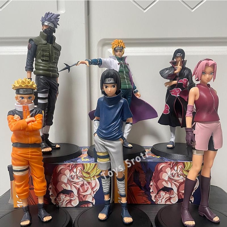 May include: A collection of six anime character figurines standing on black circular bases. The figures include characters in orange, green, blue, and black outfits, with one character wearing a long black coat with red cloud patterns and another in a pink top.