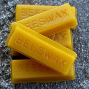 May include: Four rectangular blocks of yellow beeswax, stacked on top of each other. Each block has the word "BEESWAX" embossed on the top.
