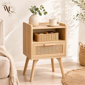 May include: A light wood nightstand featuring an open top shelf and a single drawer with a woven cane front panel. The nightstand stands on four tapered legs and holds a ribbed white vase with greenery and a white ceramic mug on its top surface.