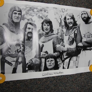 May include: A black and white poster featuring five individuals dressed in medieval chainmail and tunics, with one person positioned in the foreground. The text "Monty Python and the Holy Grail" is printed at the bottom center of the rectangular poster.