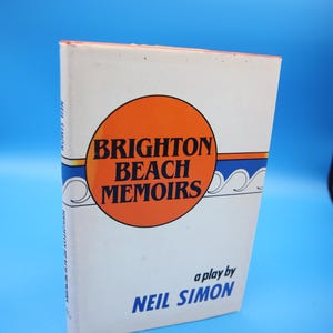 May include: A book titled "Brighton Beach Memoirs" by Neil Simon. The cover features an orange circle with the title, blue and white wave designs, and the author's name. The book is set against a blue background.
