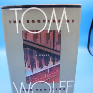 May include: A hardback book titled "Tom Wolfe The Bonfire of the Vanities." The cover shows a cityscape reflected in a window, with the author's name and book title in large white letters. The book is by the author of "The Right Stuff."