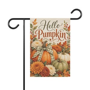 May include: A rectangular garden flag hanging on a black metal stand. The flag features the text Hello Pumpkin in brown script, surrounded by orange, white, and green pumpkins, autumn leaves, red berries, and white and orange chrysanthemums.