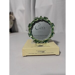 May include: A round picture frame featuring a border of light green faceted glass stones. The frame displays the text Carr Frames and 3.5 x 3.5. It rests on a cream-colored cardboard box with text including Burnes of Boston and Made in China.