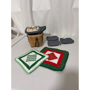 May include: A woven wooden basket with a snowman-themed lid, accompanied by several quilted fabric pot holders. The pot holders feature various patterns including green and white stripes, red and white plaid, and dark blue polka dots.