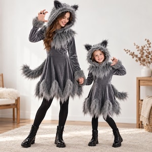 May include: Two grey velvet dresses featuring long sleeves, hoods with attached ears, and faux fur trim along the hood, cuffs, and hem. Each dress includes a matching faux fur tail attached to the back, paired with black leggings and black boots.