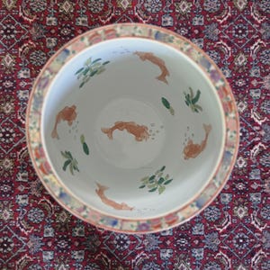 May include: A round ceramic planter with a white interior featuring hand-painted orange koi fish and green aquatic plants. The rim is decorated with a colourful, intricate pattern of floral and geometric motifs in shades of red, blue, and gold.