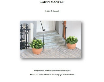 May include: A miniature tutorial for creating a 1:12 scale 'Lady's Mantle' perennial plant. The image shows a close-up of two miniature potted plants with green leaves and brown pots, placed on a stone walkway.