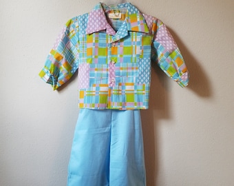 May include: A two-piece outfit for a child, featuring a short-sleeved button-up shirt with a patchwork design in shades of blue, green, pink, and orange. The shirt has a collar and a button closure. The outfit also includes a pair of light blue pants.