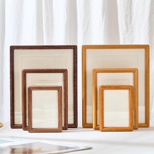 Op de afbeelding: Een verzameling van zes rechthoekige houten fotolijsten gerangschikt in twee groepen van drie, met variërende formaten en twee verschillende houttinten, met donkere walnootkleurige lijsten links en lichtere eikenkleurige lijsten rechts.