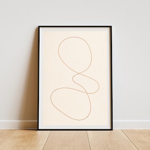 Puede incluir: Una impresión de arte mural enmarcada que presenta una línea fina y continua de color cobre que forma una figura abstracta, orgánica y con bucles sobre un fondo de color crema sólido. La obra está dentro de un marco rectangular negro fino.