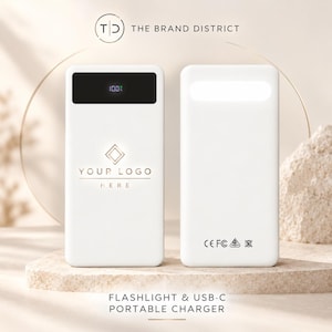 May include: A white portable charger with a black digital display showing 100% battery, a central logo placeholder, and a built-in flashlight. The text reads THE BRAND DISTRICT and FLASHLIGHT & USB-C PORTABLE CHARGER with CE, FC, and recycling icons.