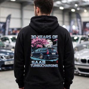 May include: A black hooded sweatshirt featuring a graphic on the back of a dark station wagon parked under a pink cherry blossom tree. The text reads 30 YEARS OF SAAB TURBOCHARGING in a light blue font, with a stylized sun and building in the background.