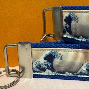 May include: Two key fobs with a blue and white wave pattern, reminiscent of the iconic "Great Wave off Kanagawa" artwork. The key fobs have a blue fabric base and a silver-colored metal key ring.
