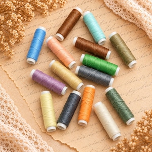 Peut inclure: Une collection de quinze petites bobines de fil à coudre de différentes couleurs, notamment bleu, marron, pêche, vert, jaune, violet, gris, orange et blanc. Chaque bobine possède un noyau en plastique blanc et est disposée en désordre.