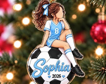 May include: A flat acrylic Christmas ornament featuring a brown-haired soccer player in a light blue jersey with the number 8, sitting on a black and white soccer ball. The ball is personalized with the name Sophia and the year 2026.
