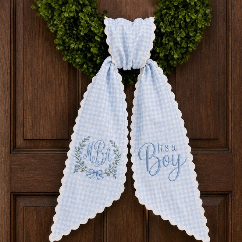 May include: A light blue and white gingham fabric bow with scalloped edges. The left tail features an embroidered floral wreath surrounding the letters MBA, while the right tail displays the embroidered text It's a Boy in blue script.