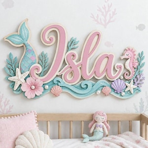 Puede incluir: Un letrero de madera para pared con el nombre Isla en grandes letras cursivas de color rosa. El diseño incluye una cola de sirena azul, un caballito de mar rosa, estrellas de mar blancas, conchas rosas y moradas y una flor rosa.