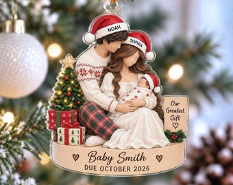 May include: A flat acrylic Christmas ornament featuring a family of three wearing Santa hats labeled Noah, Sophia, and a baby. The scene includes a decorated tree, wrapped gifts, and a sign reading Our Greatest Gift and Baby Smith October 2026.