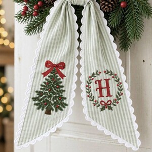 Peut inclure: Un nœud décoratif en tissu à rayures verticales vert clair et blanc avec des bords festonnés blancs. Un pan présente un sapin de Noël brodé avec un nœud rouge, l'autre une lettre H rouge entourée d'une couronne de feuilles vertes.