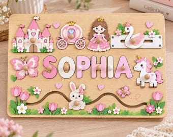 May include: A rectangular wooden puzzle board featuring the name SOPHIA in large pink letters. The board is decorated with a castle, carriage, princess, swan, butterfly, unicorn, and rabbit, all accented with small wooden knobs and flowers.