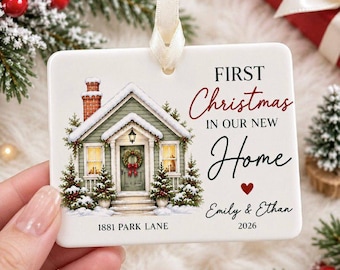 May include: A rectangular white ceramic ornament with a cream ribbon, featuring a snowy house illustration, the text "FIRST Christmas IN OUR NEW Home", "Emily & Ethan", "1881 PARK LANE", and "2026" with a small red heart icon.