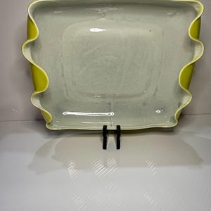 May include: A rectangular ceramic serving dish with a glossy, light-colored interior and a vibrant, chartreuse-green exterior. The edges of the dish feature a distinct, wavy, ruffled design that creates a soft, undulating border around the perimeter.