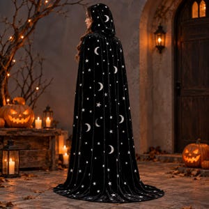 May include: A floor-length black hooded cloak featuring a repeating pattern of white crescent moons and stars. The garment is made of a velvet-like fabric and drapes from the shoulders to the ground, covering the back and sides of the wearer.