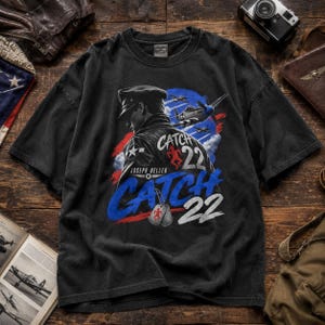 May include: A black short-sleeve t-shirt featuring a graphic of a pilot in a leather jacket, military aircraft, and the text Catch 22 by Joseph Heller. The design includes a red running figure icon, blue and white accents, and two metal dog tags.