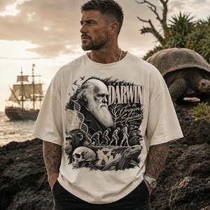 Puede incluir: Una camiseta de manga corta color hueso con un estampado gráfico en negro de Charles Darwin, el texto "Charles Darwin On the Origin of Species", una cadena de ADN, una secuencia de evolución humana, un cráneo, una tortuga y un velero.