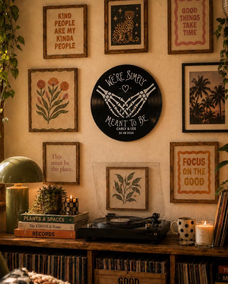 May include: A circular black vinyl record wall art piece featuring white skeletal hands forming a heart shape with the text "WE'RE SIMPLY MEANT TO BE" above and "CARLY & LEE 26 08 2026" printed below, displayed on a wall surrounded by framed prints.