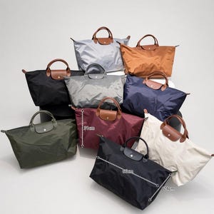 May include: A collection of nine nylon tote bags in various colours including black, olive green, burgundy, navy, beige, grey, and brown. Each bag features brown leather handles and a snap-button flap. One bag shows dimensions of 31cm height, 66cm width, and 24cm depth.