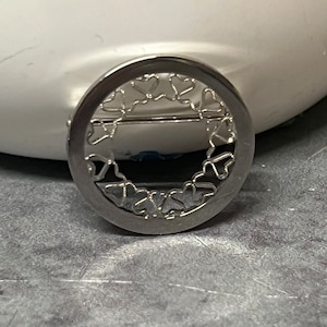 May include: A silver charm with a circular design featuring a border of cut-out hearts.