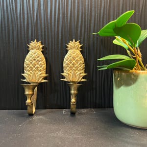 May include: Two gold pineapple-shaped wall hooks. The hooks are made of metal and have a classic design.
