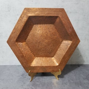 May include: A hexagonal copper tray with an embossed design, displayed on a gold metal stand.