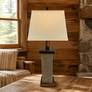 May include: A table lamp featuring a rectangular off-white fabric shade and a vertical base constructed from weathered gray wood planks. The lamp includes a dark brown wooden top and bottom plate with a central metal rod supporting the light fixture.